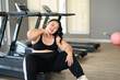 Overweight Asian young woman tired of taking a break from running or exercising sitting on treadmill machine. Asian girl in sportswear relaxing after fitness training. Weight loss workout.