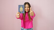 © Krakenimages.com - Smiling young hispanic woman holding a canadian passport against a pink wall gives a thumbs up.