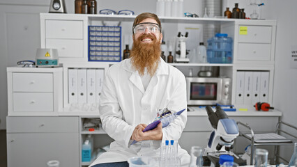 Poster - Handsome redhead male scientist working with a smile, young man captures notes indoors at medical lab, mastering scientific analysis immersed in experiment behind safety glasses