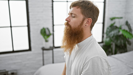 Wall Mural - Serene morning, young redhead man comfortably nestled in cozy bed, breathing in calm air. quietly awake, sitting in bedroom, serious concentration on balancing the rhythm of breath.