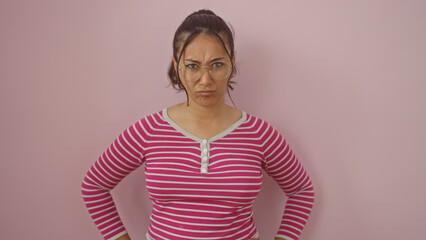 Wall Mural - A young hispanic woman with glasses posing against a pink wall, exhibiting a confident stance.