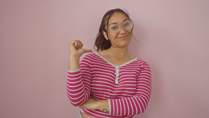 Poster - Confident young hispanic woman in a striped shirt, gesturing to herself against a pink wall.