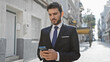 © Krakenimages.com - Handsome young hispanic man in a suit holding a smartphone on an urban city street