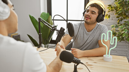 Two men engaging in a podcast conversation in a bright, modern studio setup with professional audio equipment.