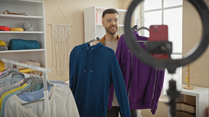 Wall Mural - A young hispanic man smiles while recording a fashion video in a well-organized room filled with stylish clothing on racks and shelves.