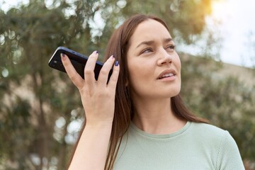 Sticker - Young beautiful woman listening audio message by the smartphone with serious expression at park