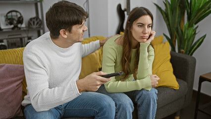 Poster - A couple lounges at home on the couch, showing a woman seemingly bored next to a man with a remote