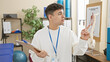 © Krakenimages.com - Young man with clipboard standing in a physiotherapy clinic, pointing to something, indoors.