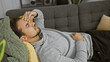Hispanic man relaxing on couch at home with hand on forehead, appearing stressed or tired.
