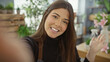 © Krakenimages.com - Smiling young hispanic woman taking a selfie in a vibrant indoor flower shop setting