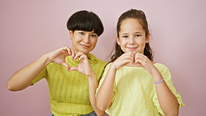 Canvas Print - Confident mother, daughter make heart gesture with hands, smiling over isolated pink background in a symbol of love, happiness and family bond.