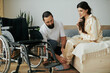 © Bliss - handsome loving man in homewear helping his disabled wife to change into pajama in bedroom at home