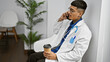 © Krakenimages.com - Handsome young latin man doctor, tattooed and serious, speaks on smartphone while relishing his espresso in clinic waiting room.