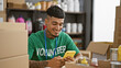 © Krakenimages.com - Handsome, tattooed young latin man cheerfully volunteering at charity center, busily texting donations details from his smartphone while sitting amidst boxes in the warehouse room