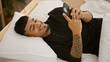 © Krakenimages.com - Confident young latin man enjoying his morning, smiling and texting on his smartphone while lying comfortably on his bed indoors, a portrait of his relaxed lifestyle at home