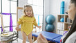 A little girl in a bright yellow outfit joyfully interacts with a woman therapist in a colorful physiotherapy clinic room.