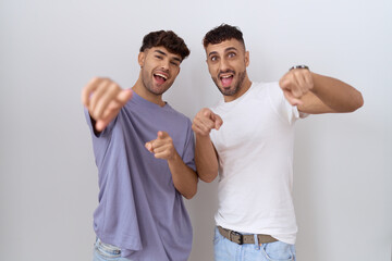 Sticker - Homosexual gay couple standing over white background pointing to you and the camera with fingers, smiling positive and cheerful