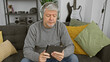 © Krakenimages.com - A mature man with headphones using a tablet on a couch in a modern living room.
