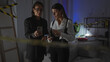 © Krakenimages.com - Two women investigators examine evidence using smartphones in the dimly lit room of a house crime scene.