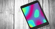 Image of tablet with colorful moving shapes on screen on wooden background