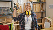 © Krakenimages.com - Beaming middle age, grey-haired woman expertly holds drill at carpentry workshop. donned headphones amplify her joy amid the timber and shavings.