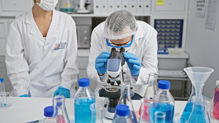 Poster - Two scientists wearing medical mask and gloves using microscope at laboratory