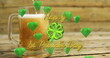 Image of st patrick's day text, shamrock and green hearts over glass of beer