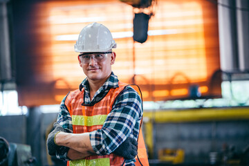 Wall Mural - Portrait of male foreman factory wearing hardhat in arms crossed looking at camera standing at the industry factory. Construction worker or builder career in positive attitude. copy space