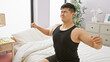 © Krakenimages.com - A young chinese man waking up and stretching in his modern bedroom at home, representing a fresh start to the day.