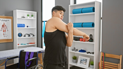 Wall Mural - An asian man stretches his arm in a modern rehabilitation clinic's gym, indicating a healthcare or physical therapy setting.