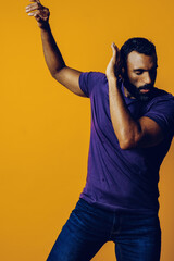 Wall Mural - portrait of a handsome sensitive young adult man dancing with purple t-shirt on a yellow background