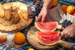 Close-up view of a cut watermelon in hands and laid out food for a picnic, selective focus. The concept of summer outdoor recreation on the weekend