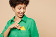 © ViDi Studio - Close up cropped young woman of African American ethnicity in green shirt casual clothes hold in hand put mock up of credit bank card into pocket isolated on plain beige background Lifestyle concept