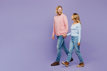 Wall Mural - Full body side view young smiling couple two friends family man woman wear pink blue casual clothes together hold hands walking going isolated on pastel plain light purple background studio portrait.