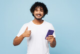 Fototapeta  - Young happy fun Indian man he wear white t-shirt casual clothes hold in hand use mobile cell phone show thumb up isolated on plain pastel light blue cyan background studio portrait. Lifestyle concept.