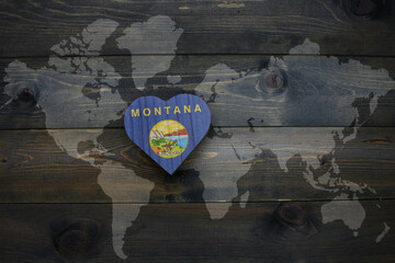 Wall Mural - wooden heart with national flag of montana state near world map on the wooden background.