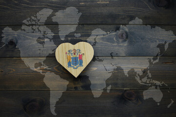 Wall Mural - wooden heart with national flag of new jersey state near world map on the wooden background.