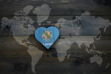 Wall Mural - wooden heart with national flag of oklahoma state near world map on the wooden background.