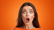 A woman with long brown hair and a surprised expression on her face. She is wearing an orange shirt. a lady looking shocked with with a bold orange oultine around her on an orange background