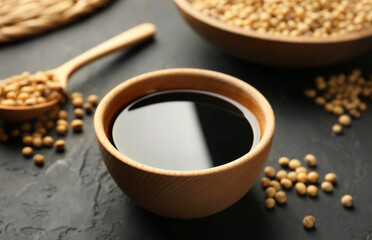 Tasty soy sauce in bowl and soybeans on black table, closeup