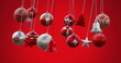 Image of multicolored baubles, stars and bells swinging against red background