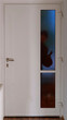 Ein Einbrecher steht in der Dunkelheit mit einer Pistole vor einer Eingangstüre und schaut durch die Glasscheibe in die Wohnung oder Haus rein

