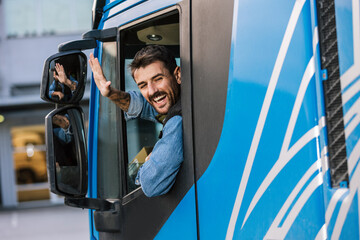 Young handsome truck driver driving a truck and waving  through the window.