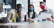 Image of social media icons over diverse colleagues wearing face masks discussing at office