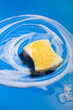 cleaning sponge wiping foam soap suds on blue background, household washing concept