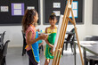 In school, in art class, biracial and a Caucasian girl, both young, are painting