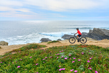 Wall Mural - nice senior woman riding her electric mountain bike at the rocky and sandy coastline of the atlantic ocean in Porto Covo, Portugal, Europe