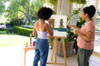 Biracial mother and adult daughter are painting outside, surrounded by greenery, at home