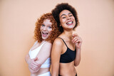 Fototapeta Londyn - Beauty image of two young smiling and happy women with different body posing in studio for a body positive photoshooting. Mixed female models in lingerie on colored backgrounds. 