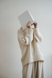 Fototapeta Tulipany - Woman in white wearing hiding face with book, album or notebook. Reading, studying concept. Neutral beige color. Blank cover sheet mock up with copy space